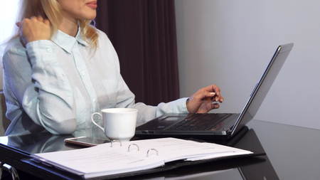A woman reads important documents in a folder and types it into a laptop