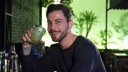 Handsome cheerful young bearded man drinking at the local bar