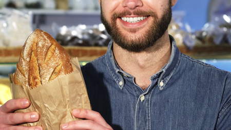 Cropped close up f a bearded man smiling holding a loaf of fresh breadの写真素材