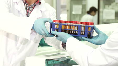 A close-up of the hands of a lab technician who passes the test tubes with analyzes to his colleague