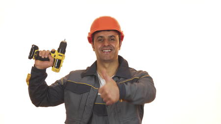 Happy mature industry worker in hardhat showing thumbs up holding drill