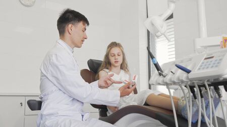 Little girl talking to her dentist sitting in dental chair ready for teeth checkupの写真素材