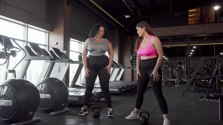 Two lovely plus size female athletes squatting with kettlebells at the gymの写真素材