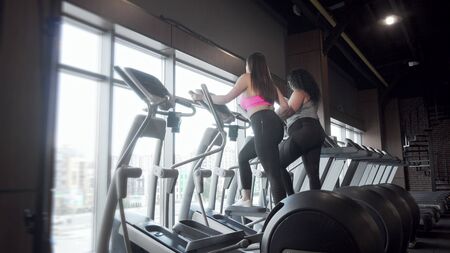 Rear view full length shot of two plus size women exercising on elliptical trainerの写真素材