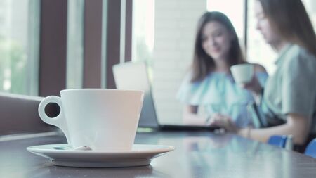 Cup of coffee on the table of two students working on a project on backgroundの写真素材