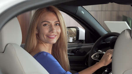 Gorgeous happy woman sitting in expensive new car smiling to the camera