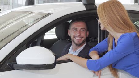 Handsome man talking to his wife while choosing new car at dealership salonの写真素材