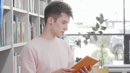 Young man enjoying reading a book at the library