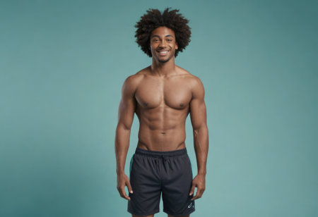 A shirtless man with afro hair smiling confidently, showcasing his athletic physique against a blue backdrop.の素材