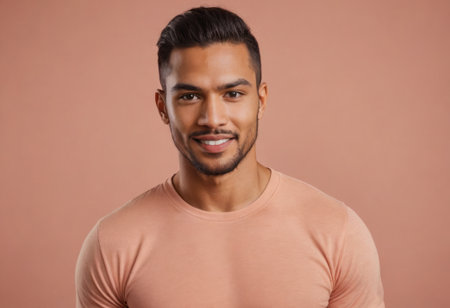 A handsome man in a peach t-shirt gives a confident smile. The soft peach backdrop creates a cohesive look.の素材