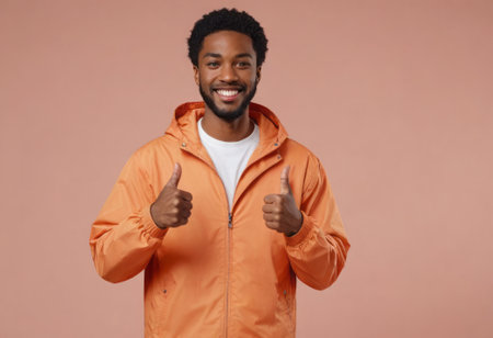 A smiling man in an orange jacket shows thumbs up. His casual look and friendly demeanor suggest approachability and positivity.の素材