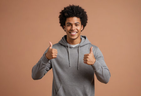 A youthful man in a grey hoodie gives double thumbs up. His exuberant smile and curly hair add to his lively persona.の素材