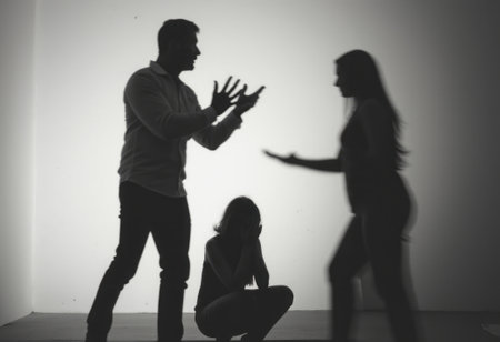 In a stark, shadowy setting, a man and a woman engage in a heated argument, their silhouettes sharply defined against a bright backdrop. A third figure, a woman crouched in despair, adds a poignant layer of emotion, capturing the intensity of conflict and the weight of unspoken feelings.の素材