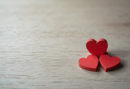 Three charming red hearts are artfully arranged on a smooth wooden surface, radiating warmth and affection. Their playful positioning evokes a sense of love and connection, inviting viewers to reflect on the beauty of relationships and heartfelt emotions.の素材