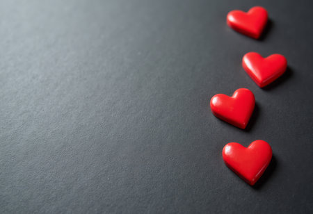 A delightful arrangement of four glossy red hearts is set against a sleek, dark background, creating a striking contrast that draws the eye. The vibrant hearts, symbolizing love and affection, evoke feelings of warmth and joy, making this image perfect for expressing heartfelt emotions.の素材
