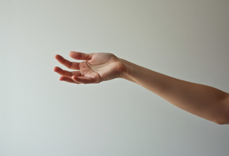 An elegant hand extends gracefully against a soft, neutral background, embodying a sense of openness and invitation. The delicate fingers, slightly curled, suggest a moment of connection, evoking feelings of warmth and welcome in a serene atmosphere.の素材