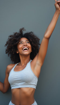 A vibrant young woman with curly hair beams with joy, raising her arm triumphantly against a sleek gray background. Her expression radiates happiness and confidence, embodying the spirit of achievement and positivity.の素材
