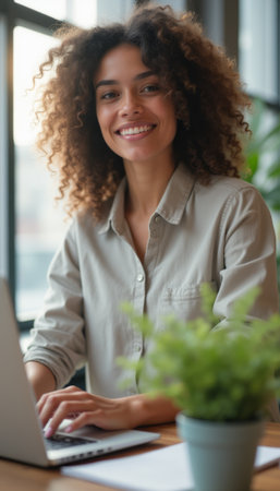 Smiling woman working on a laptop in a bright, cozy workspaceの素材