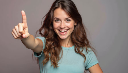 Cheerful woman pointing upwards with a bright smileの素材
