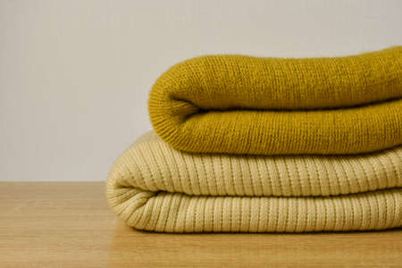 Stack of folded knitted sweaters on wooden table, closeup. Space for text