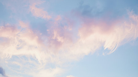 Soft pastel-colored clouds float across a clear blue sky, captured in natural light during sunset, evoking calm and dreamlike feelings. High quality photoの素材