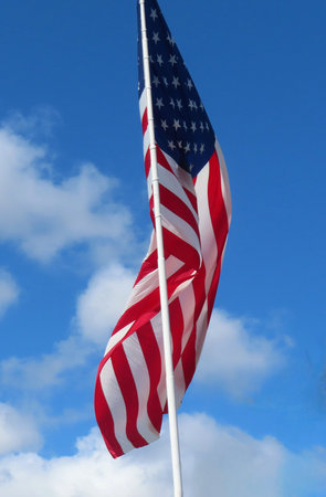 American flag waving in the wind against a blue sky with white clouds