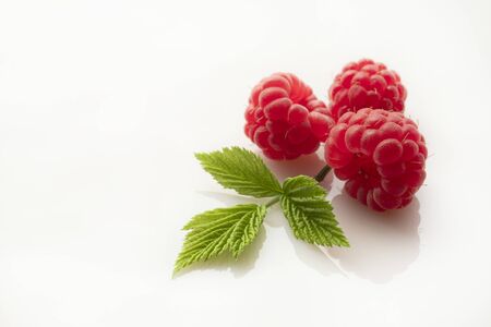 Ripe juicy raspberries and a green leaf on a white background.