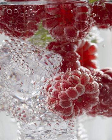 Fresh raspberries in a glass of mineral water and ice cubes on a white background.の写真素材