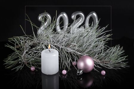 Christmas mysterious composition in dark colors. burning candle, pink ball on the background of fir branch and asilver 2020の写真素材