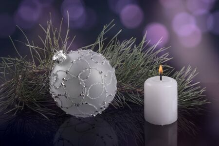 white Christmas ball and a white candle with spruce twig on background of purple highlights blurredの写真素材