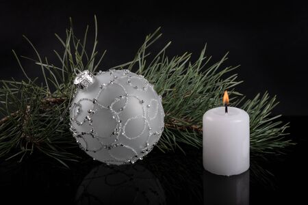 White Christmas ball and white candle with fir twig on black backgroundの写真素材