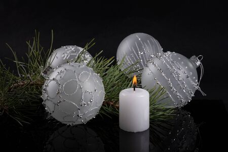 White candle and Christmas balls lie near Christmas tree on dark backgroundの写真素材
