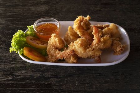 Fried prawns in breadcrumbs with sauce on white plate. seafood on dark background.