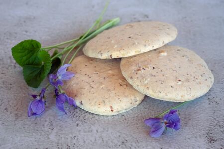 Nutty homemade cookies lying in a pile on the table with purple violetsの写真素材