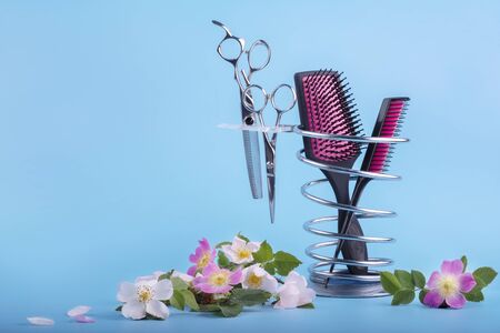 Hairdressing tools on a metal stand decorated with delicate pink flowers on a blue backgroundの写真素材