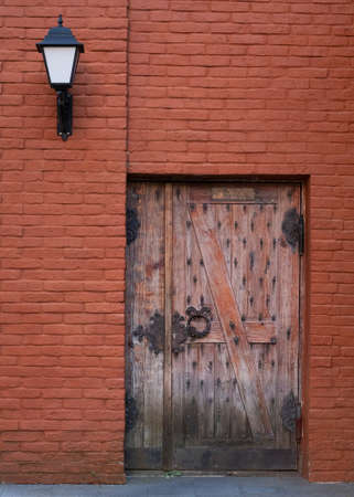 Antique wooden door with metal hinges on a red brick wall