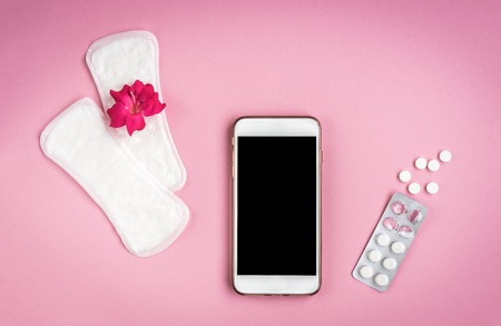 Woman hygiene protection. Sanitary pads with pain pill, pink rose and mobile phone on pink background. Menstrual cycle tracking.の写真素材