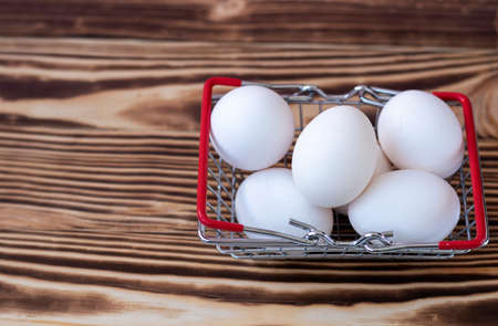 white chicken eggs in a grocery basket stand on a burnt wooden background.の写真素材