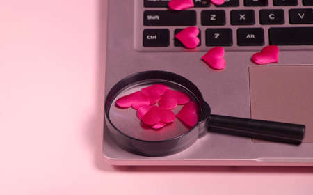 Red heart on the computer keyboard, magnifying glass with handle.