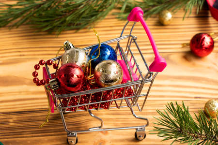 Present box and Christmas balls in the miniature shopping cart on wooden tableの写真素材