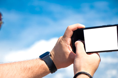 male Hand holding smartphone isolated on sky background. template for design.の写真素材
