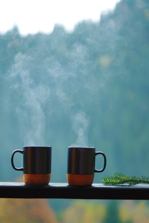 Two steaming cups of coffee on a wooden balcony with mountain viewの写真素材