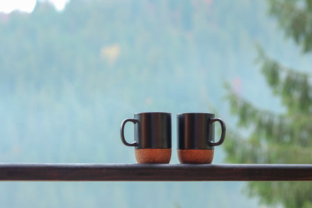 Two steaming cups of coffee on a wooden balcony with mountain viewの写真素材