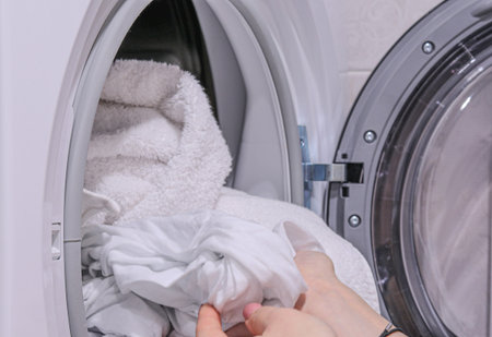 Female hand taking clean white clothes out of a washing machine drum.