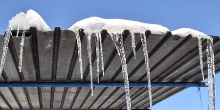 Icicles hanging from the roof. Sharp icicles hang down on a sunny winter day. Horizontal color photo.の写真素材