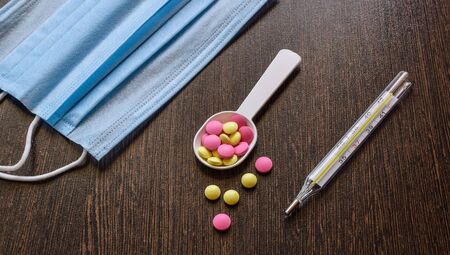 Medical drugs on a dark background. Thermometer, medical mask and colored pills. Treatment for a cold.の写真素材