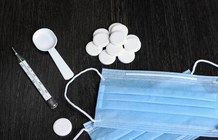 Medication on a dark background. Thermometer, pills, medical mask.