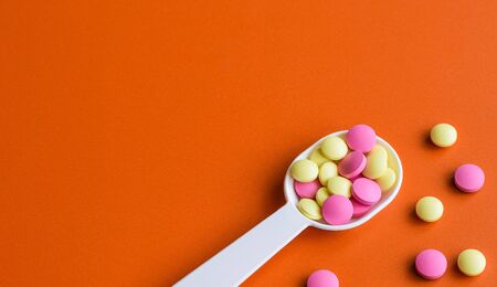 Colored pills on the table. Medical preparations on an orange background. Place for text.の写真素材
