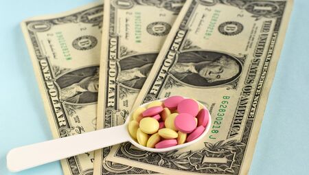 American dollar colored pills in a medical spoon on blue