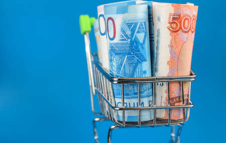 Russian rubles in a trolley on a blue background. Grocery basket and Russian rubles. Russian currency. Side view. Selective focus.の写真素材